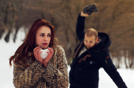 Young lovers fighting. Sad woman holding snow heart in hands while her boyfriend is angry in the background.の写真素材
