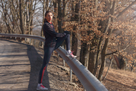 Woman doing stretching before jogging in sunny autumn day
