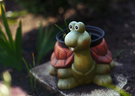 Funny ceramic turtle in garden, holding hotchpotch with plantsの写真素材