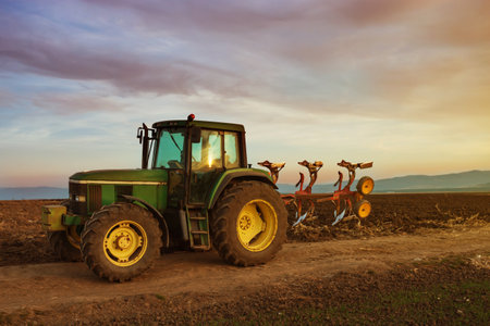 Green tractor on field at sunset after plowingのeditorial素材