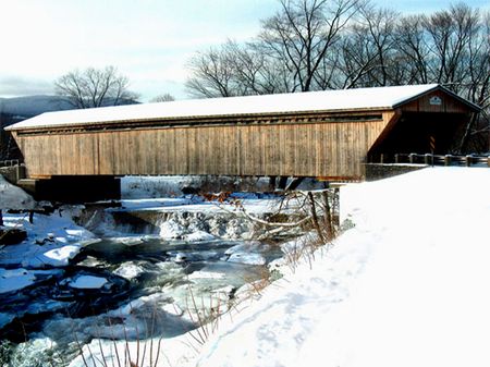 snow covered Long wooden covered bridge over partially frozen waterfallの写真素材