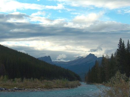 rocky mountain range with trees and stream in the foregroundの写真素材