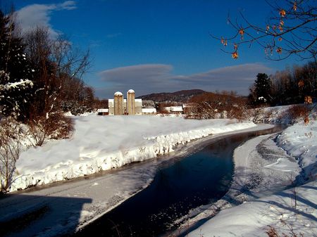 snow covered farm buildings in meadow by riverの写真素材