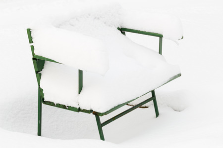 Snow-covered park bench during snowy winter after heavy snowfallの写真素材