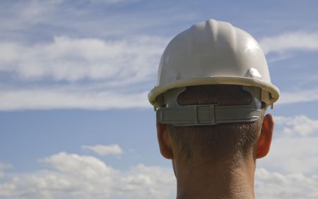 man with back to camera looking out over grass wearing a hardhat