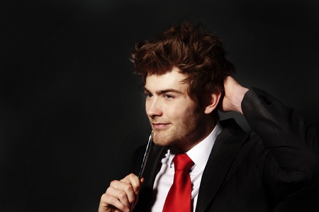 low key image of a young businessman holding a pen up to his face