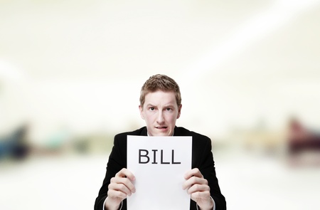 man in a suit sat at a desk look at a  piece of paper with the words bill printed on itの写真素材