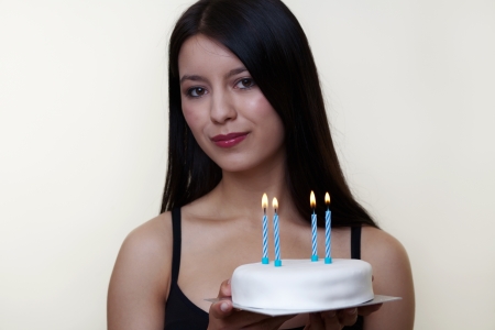 young woman holding up a birthday cake with the candle alight