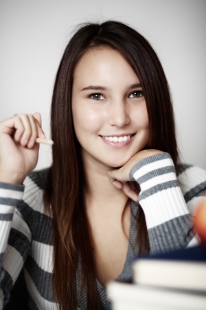 young smiling woman holding a pencil working hard with a pile of books in front of her and a apple in front of her in case she gets hungryの写真素材