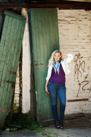 fashion shot of woman standing by a broken large garage wooden door の写真素材