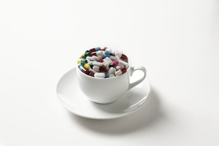 many pills shot in a cup and saucer on a white backgroundの写真素材
