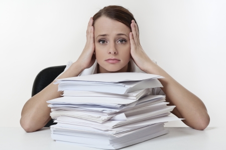 A stressed female with her head in her hands, sitting at her desk with a large  pile of paper work  stacked in front of her. の写真素材