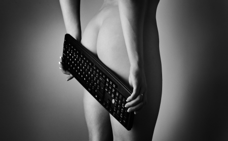 back side of nude bum with her hand holding a computer keyboard covering part of her bumの写真素材