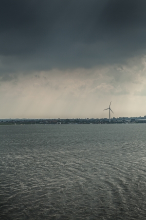 View of singular wind turbine across rippling water, Essex, England