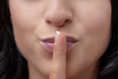 close up image of young woman with finger on her mouth to indicate that you should be quiet 