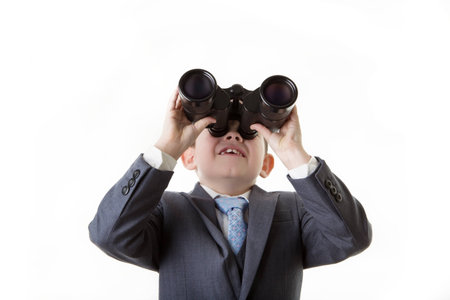 young boy dressed up in a sharp business suit looking through binocularsの写真素材