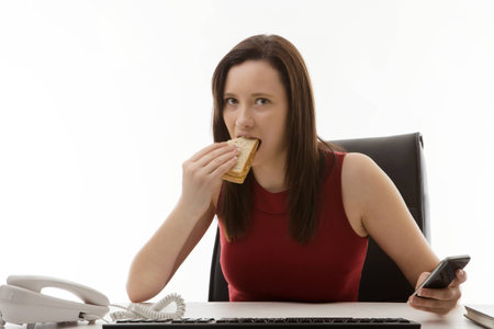 woman sitting at her desk in the office eating a sandwich as well as working on the goの写真素材
