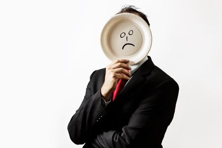 businessman holding a papper plate up to his face with a sad face draw on plateの写真素材