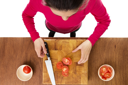 woman chopping up tomatoes on a wooden chopping board taken from a birds eye view from aboveの写真素材