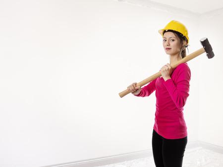 woman holding a sledgehammer and wearing a hard hat about to smash somethingの写真素材