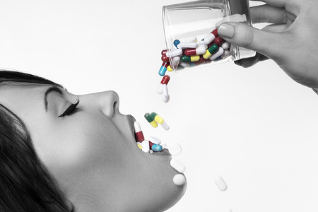 woman pouring a glass full of pill down her throatの写真素材