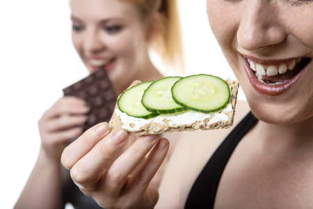 two fitness woman one eating healthy and the other is eating chocolateの写真素材