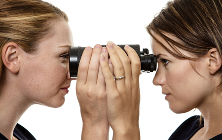 Two business woman looking through the same pair of binocularsの写真素材