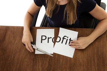 woman shot from above cutting paper in half with the word profit written on the paperの写真素材