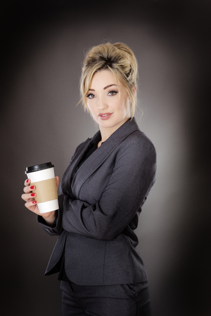 business woman drinking from a take away paper cup shot in the studio on a gray backgroundの写真素材