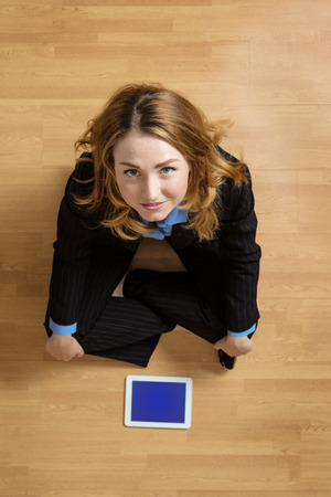 Shot taken from above of a woman sitting cross legged on the floor with her tablet computer infront of her, whilst on the phoneの写真素材