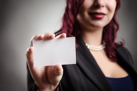 Close up studio shot of a business woman holding a blank card in her outstretched right handの写真素材