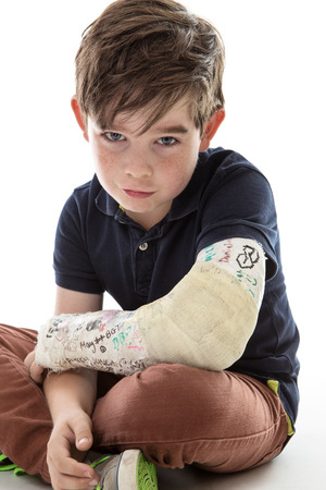 Young boy is sitting down and unable to join in because he has broken his armの写真素材