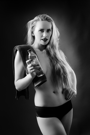 studio black and white image of topless woman with long hair covering her breasts holding a bottle of water with a towel over her shoulderの写真素材
