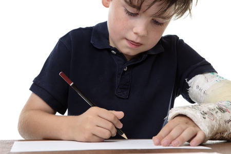 young boy drawing a picture , whilst he has a broken left arm
