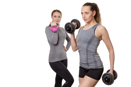 two fitness woman working out one using dumbbells the other a kettebellの写真素材