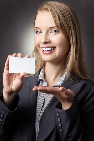 Studio shot of a pretty business model holding a small, white, blank sign in her right hand.  shot on a grey background.の写真素材