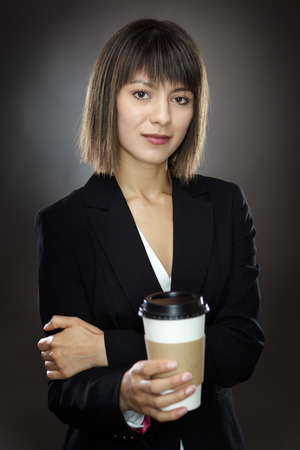 portrait of young sharply dressed business woman holding a take away cup shot in the studio low key lighting on a gray backgroundの写真素材