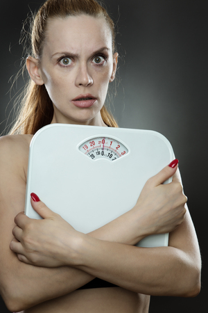 woman shot in the studio, low key lighting holding weight scales close to her chest looking worriedの写真素材