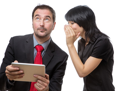Studio shot of male and female co-workers discussing working she is whispering something into his...