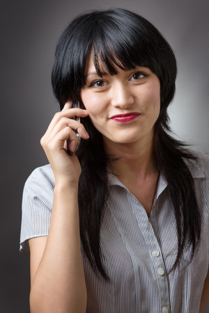 Close up portrait shot of an attractive young business woman talking on her mobile phone.  Shot on a grey background.の写真素材