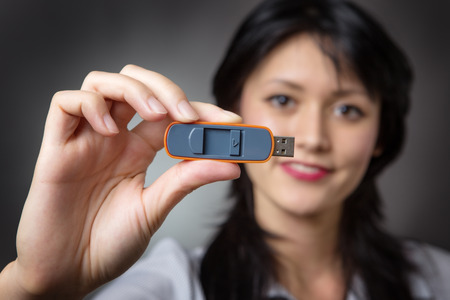 Head and shoulders studio shot of a pretty business model holding a usb memory stick out infront of her,  shot on a grey backgroundの写真素材