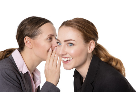 Close up shot of two happy, pretty business women, sharing a secret and whispering in each others ear.  Isolated on a white backgroundの写真素材