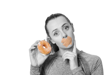 woman with first aid plaster over mouth unable to eat a donut