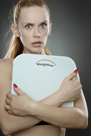 woman shot in the studio, low key lighting holding weight scales with the words weightloss printed on the scales diskの写真素材