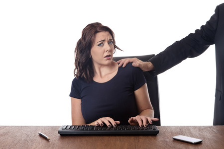business woman sitting at her desk with a male work colleague touching her on the shoulderの写真素材