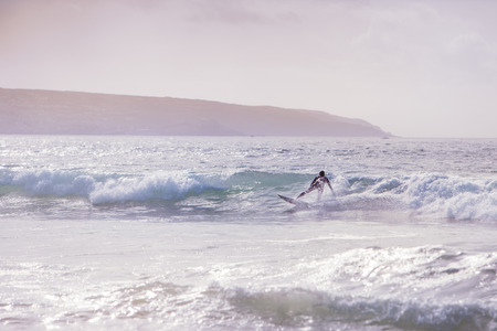 Surfer riding a wave, wearing a wetsuit at godrevy beach in cornwall uk.