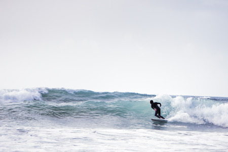Surfer riding a wave, wearing a wetsuit at godrevy beach in cornwall uk.
Do not have model release but face has been  darken and used the liquefy tool in photoshop to change the features of the face.の写真素材