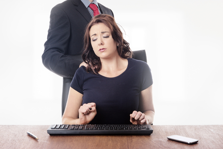 business woman sitting at her desk with a male work colleague touching her on the shoulderの写真素材