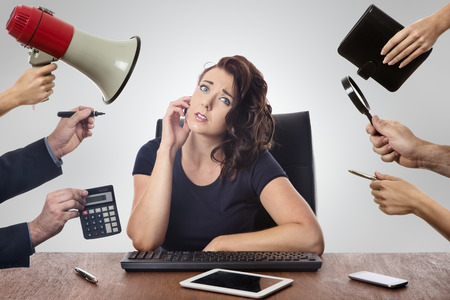 business woman sitting at desk surrounded by many hands holding objectsの写真素材
