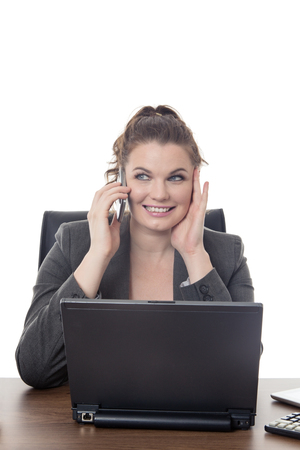 Happy business woman sitting at her desk having a good good conversation on a mobile phoneの写真素材